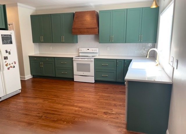 Empty kitchen with teal cabinets, white appliances, and warm hardwood floors