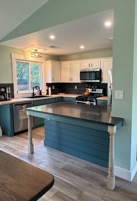 Modern kitchen with green walls, white cabinets, dark countertops, and a breakfast bar.