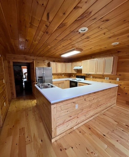 Wood-paneled kitchen with light cabinets, white countertops, and a stainless steel refrigerator and stove.