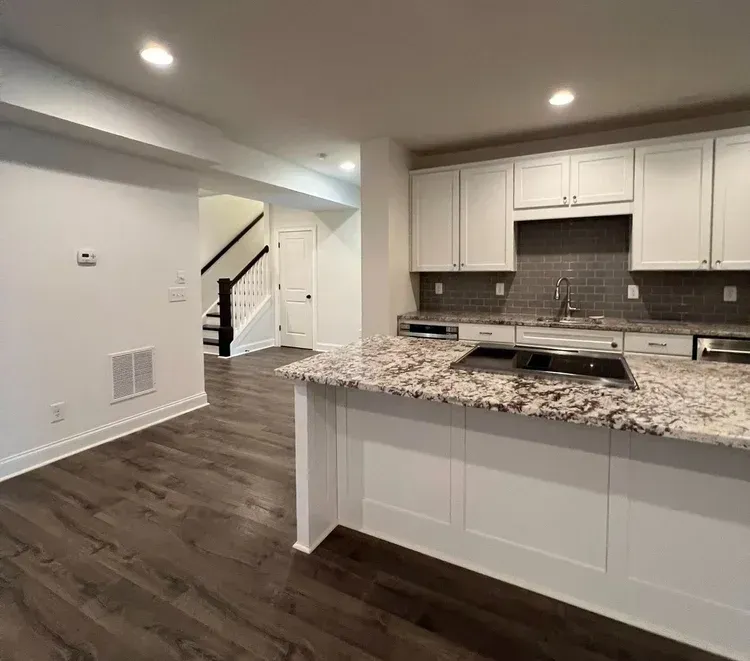 A kitchen with granite countertops and white cabinets in a basement.