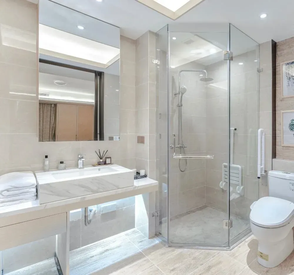 Modern bathroom with white vanity, large mirror, glass shower enclosure, and toilet.