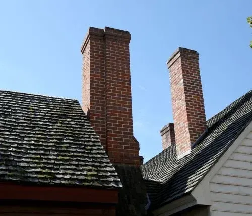 Three brick chimneys rising above dark shingled rooftops against a blue sky