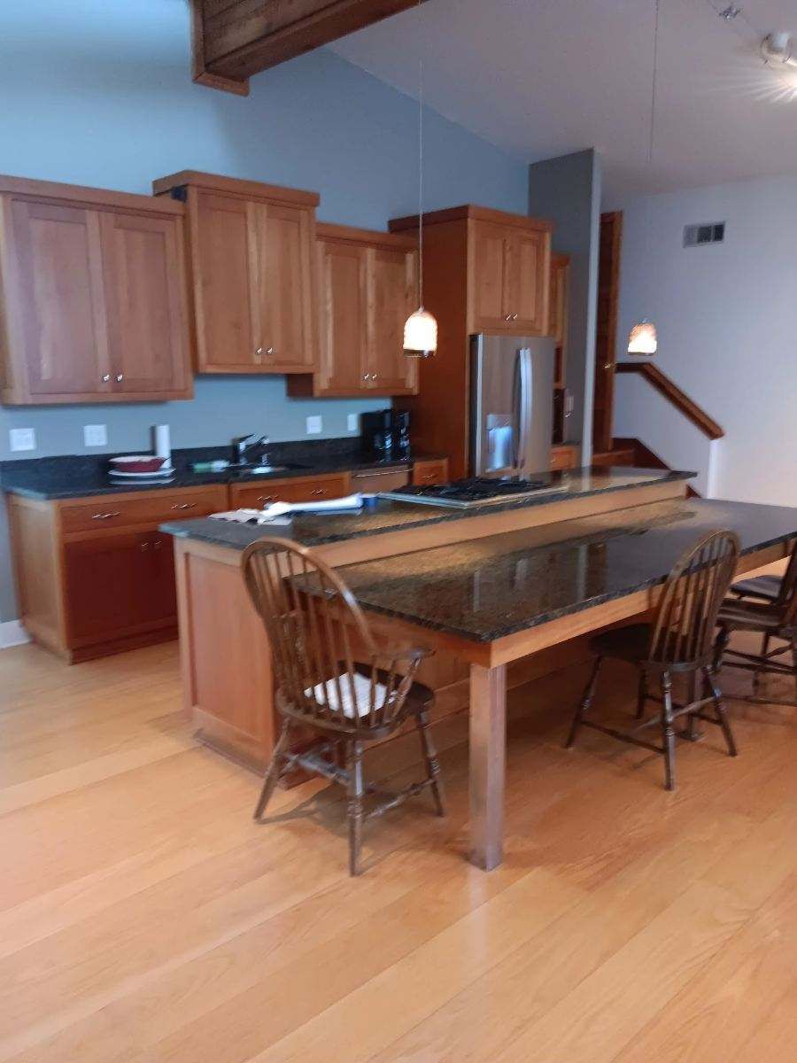 Modern kitchen with wood cabinets, island, bar stools, and hardwood floor in a bright open space