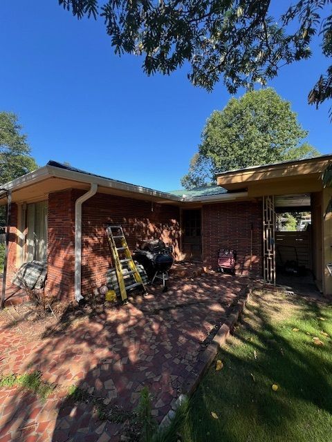 Back patio of a brick house with a ladder, motorcycle, and blue sky overhead