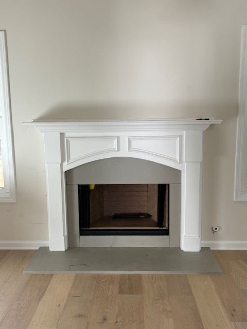 White fireplace mantel with arched opening centered on a light wood floor, flanked by wall sconces.