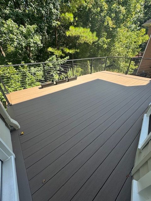 Spacious deck with brown flooring, black railing, and wooded backyard view