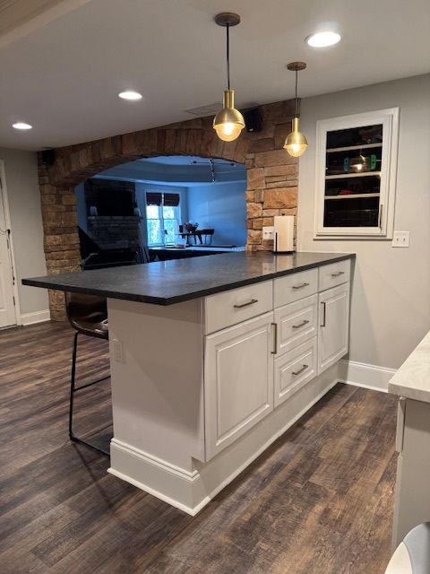 Kitchen with white island, dark countertop, hanging pendant lights, and wood flooring in an open-plan home.