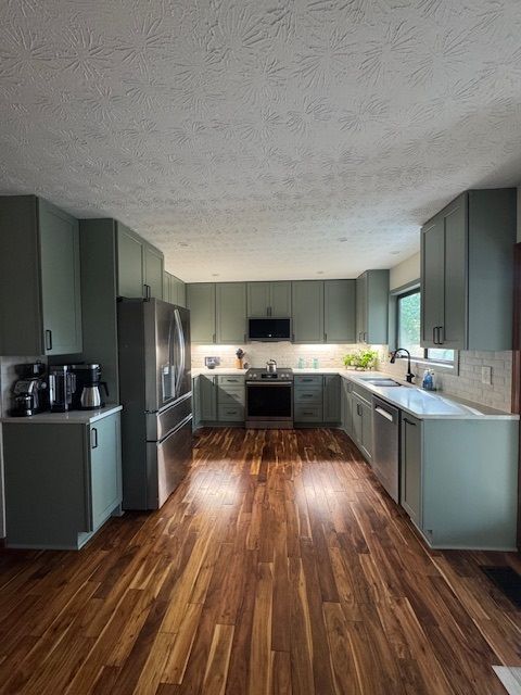 Modern kitchen with sage green cabinets, stainless appliances, and wood floors viewed from the center.