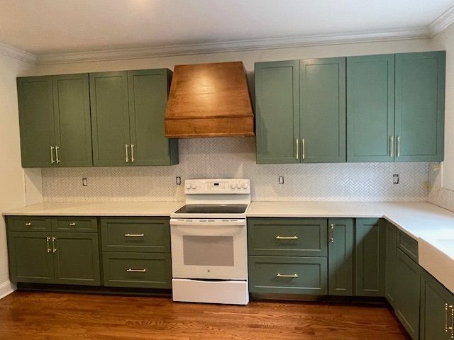 Empty kitchen with green cabinets, white stove, and wood range hood.