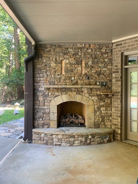 Stone outdoor fireplace on a covered patio with an arched firebox and mantel shelf