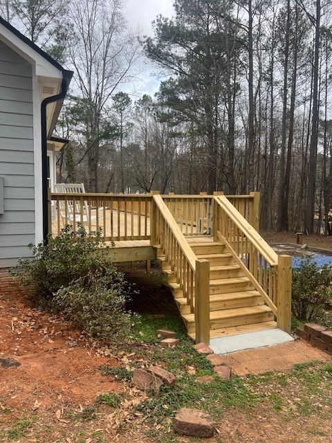Wooden deck with stairs and ramp beside a house, in a wooded yard