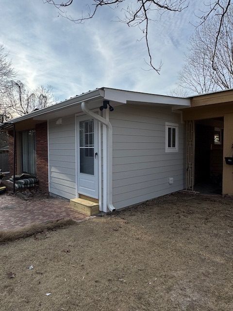 Small house exterior with white siding, a red brick wall, and a covered carport under bare trees.