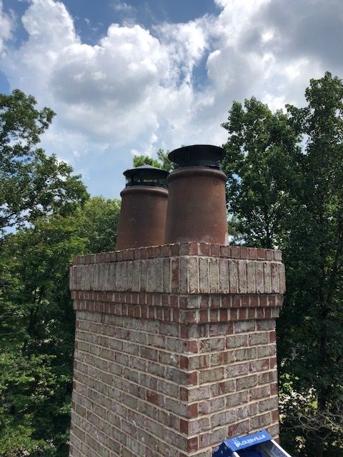 Brick chimney with two metal flues against a cloudy sky and trees