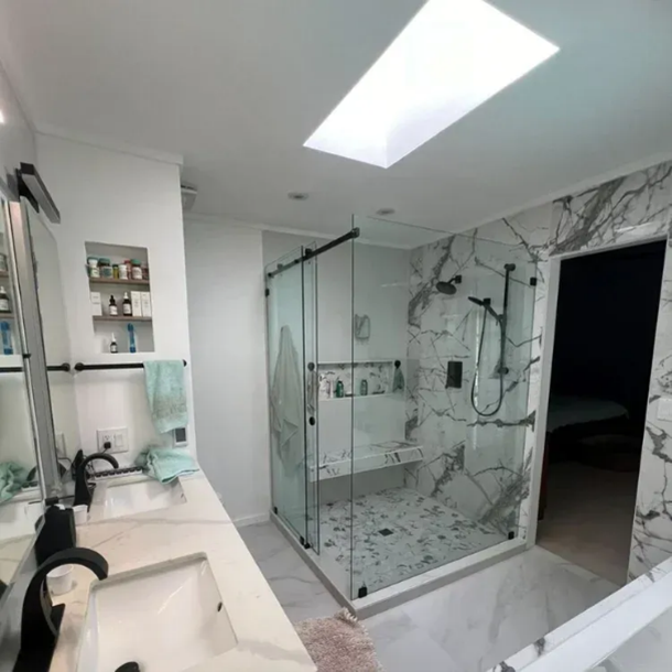 Modern bathroom with glass shower, marble tile, double sink vanity, and skylight