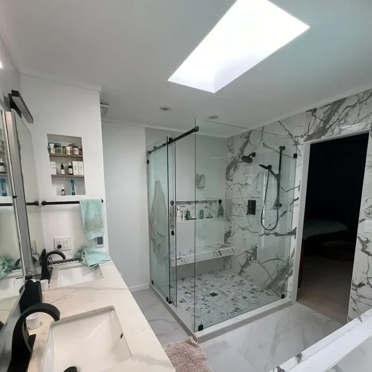 Modern bathroom with marble shower, skylight, double sinks, and glass-enclosed shower stall
