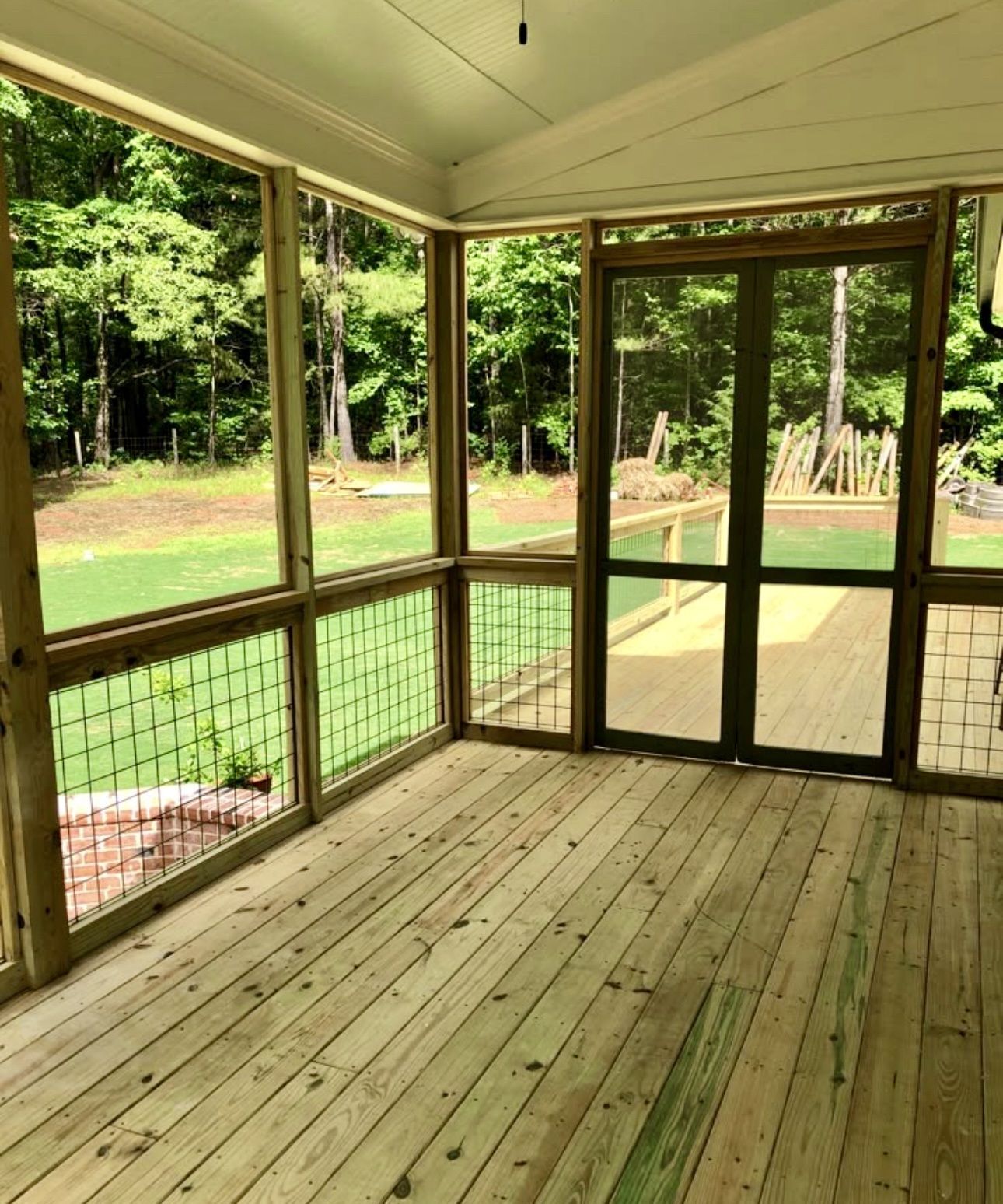 A wooden-floored screened porch featuring a glass door that opens to a green backyard with trees.