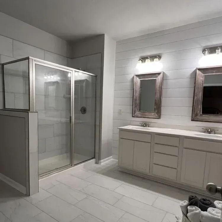 Modern white bathroom with glass shower, double vanity, and large mirrors