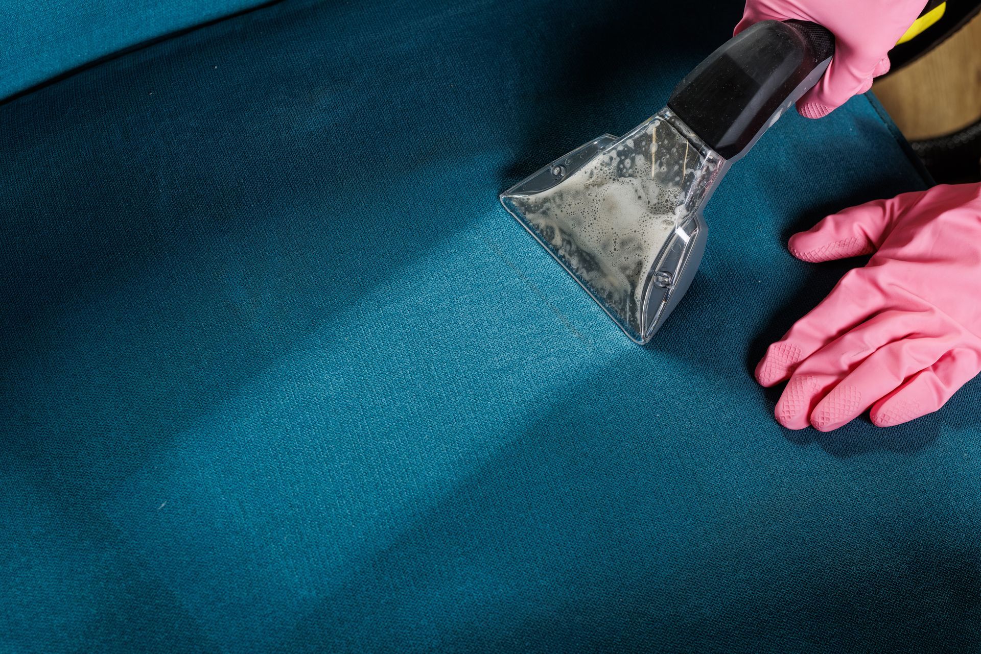 Gloved hands using a carpet cleaner on a teal carpet, removing dirt and moisture Gloved hands using a carpet cleaner on a teal carpet, removing dirt and moisture