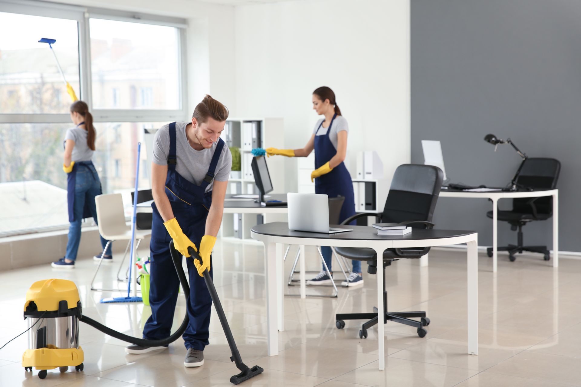 Office cleaners vacuuming and wiping a bright workspace with desks and computers Office cleaners vacuuming and wiping a bright workspace with desks and computers