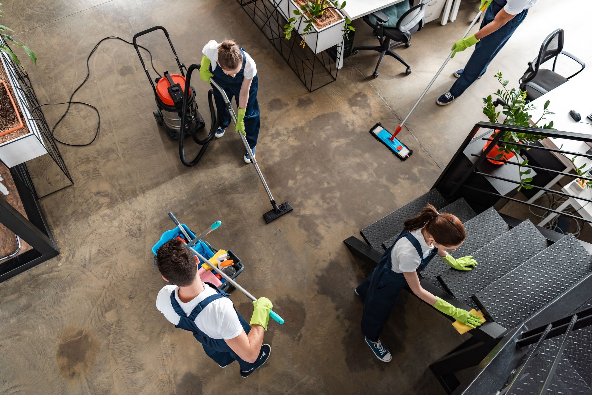 People cleaning a concrete patio with mops, vacuum, and cloths around outdoor furniture and plants