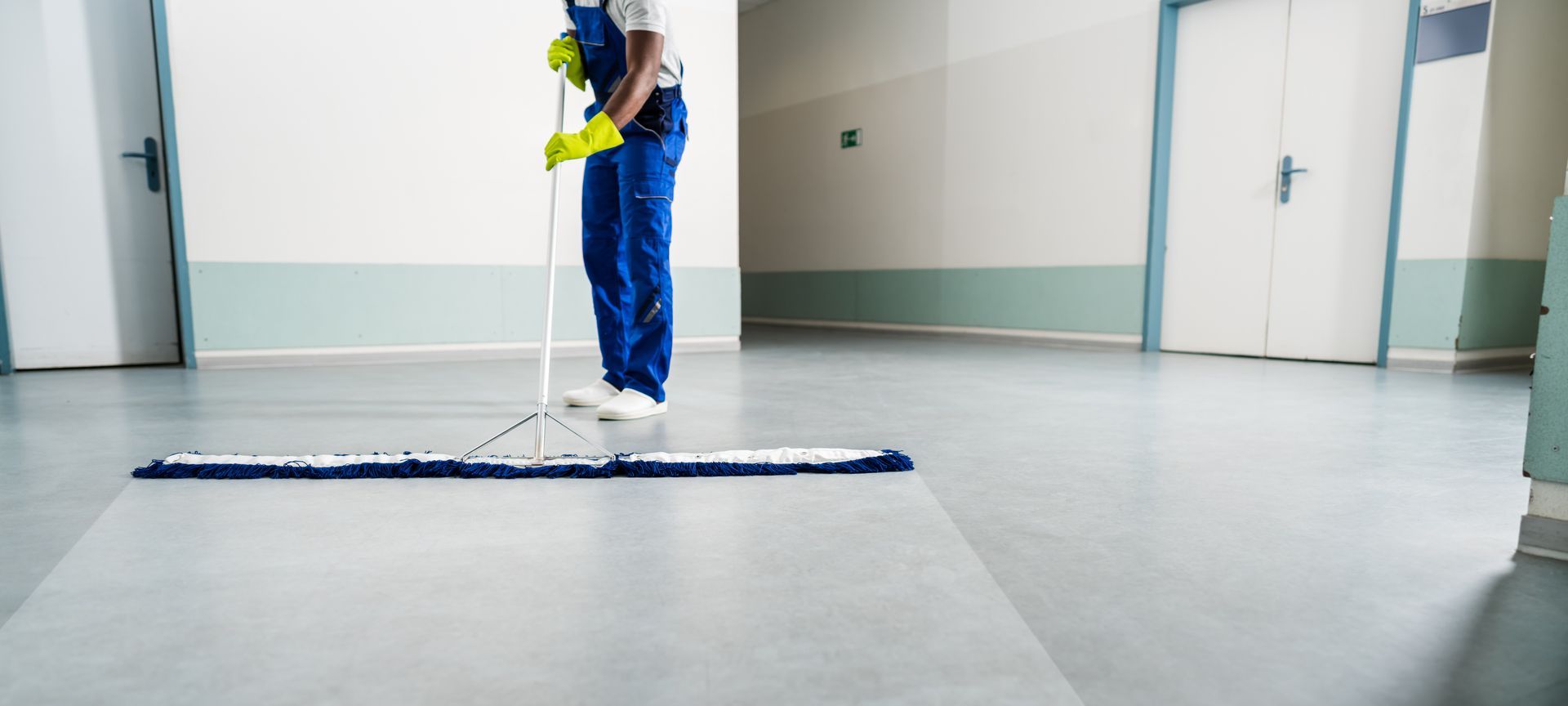 Cleaner mopping a bright office floor with a blue mop and bucket
