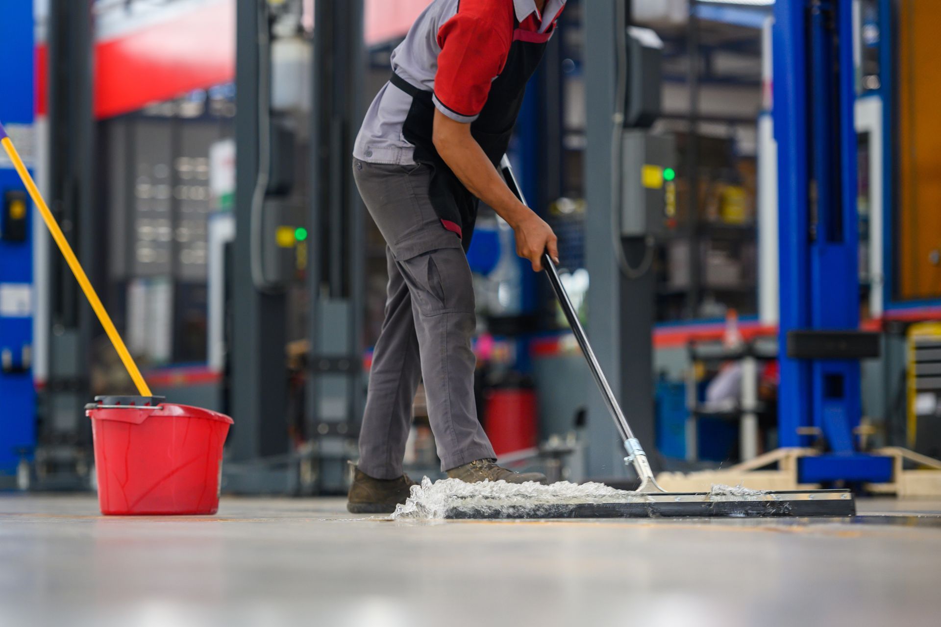 Worker mopping a factory floor beside a red bucket and cleaning cart Worker mopping a factory floor beside a red bucket and cleaning cart