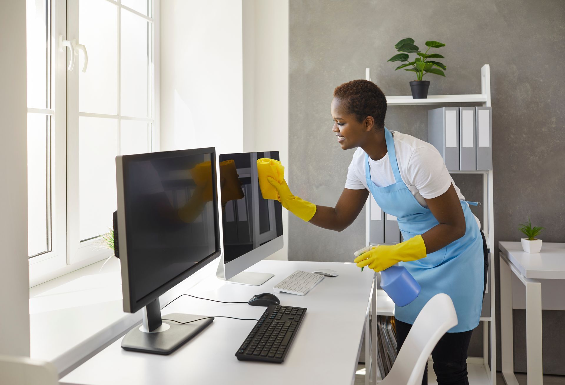 Person cleaning computer monitors with a yellow cloth in a bright office. Person cleaning computer monitors with a yellow cloth in a bright office.