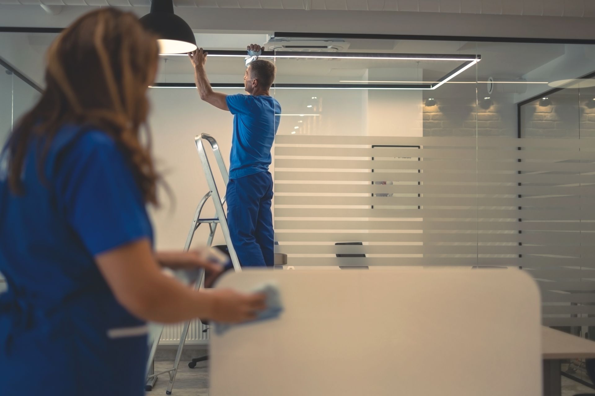 Office cleaners mopping a wet floor around desks and computers in a bright workspace
