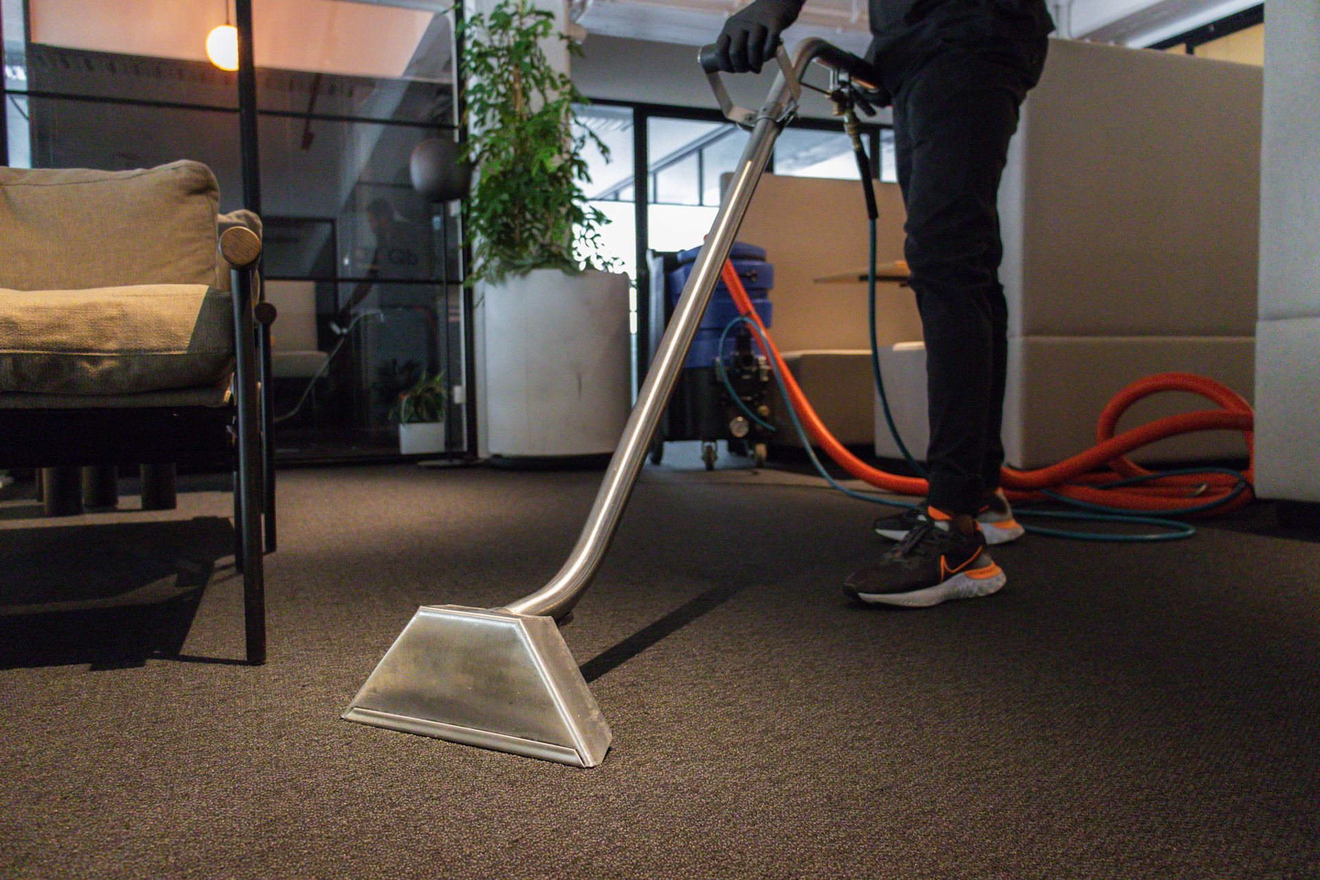 Person using a carpet cleaning wand on office carpet, with hoses and equipment visible. Person using a carpet cleaning wand on office carpet, with hoses and equipment visible.