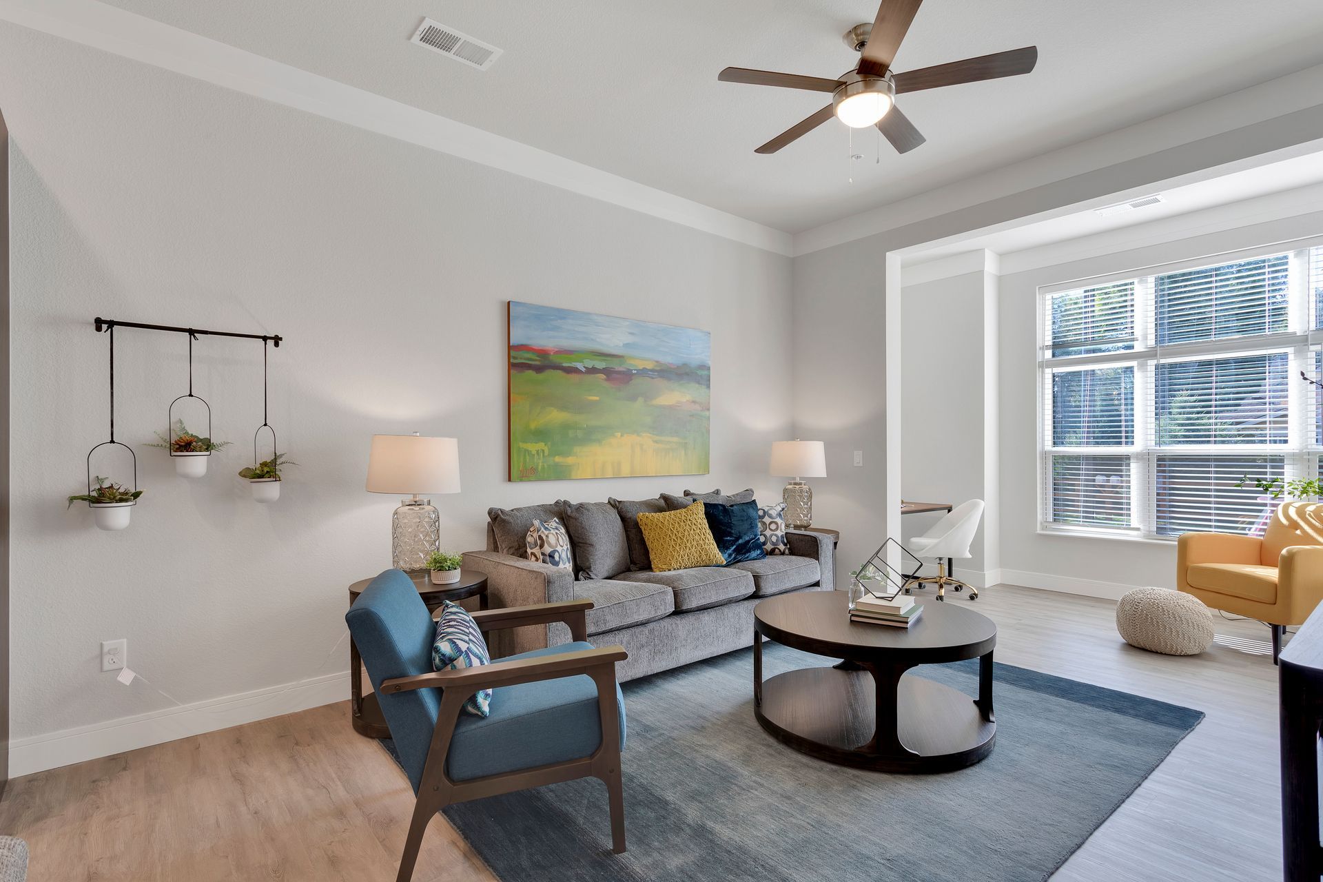 Bright living room with gray sofa, blue chair, coffee table, large window, and ceiling fan