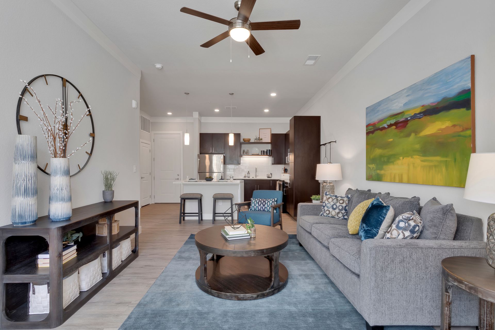 Modern living room with gray sofa, blue rug, coffee table, wall art, and open kitchen in the background