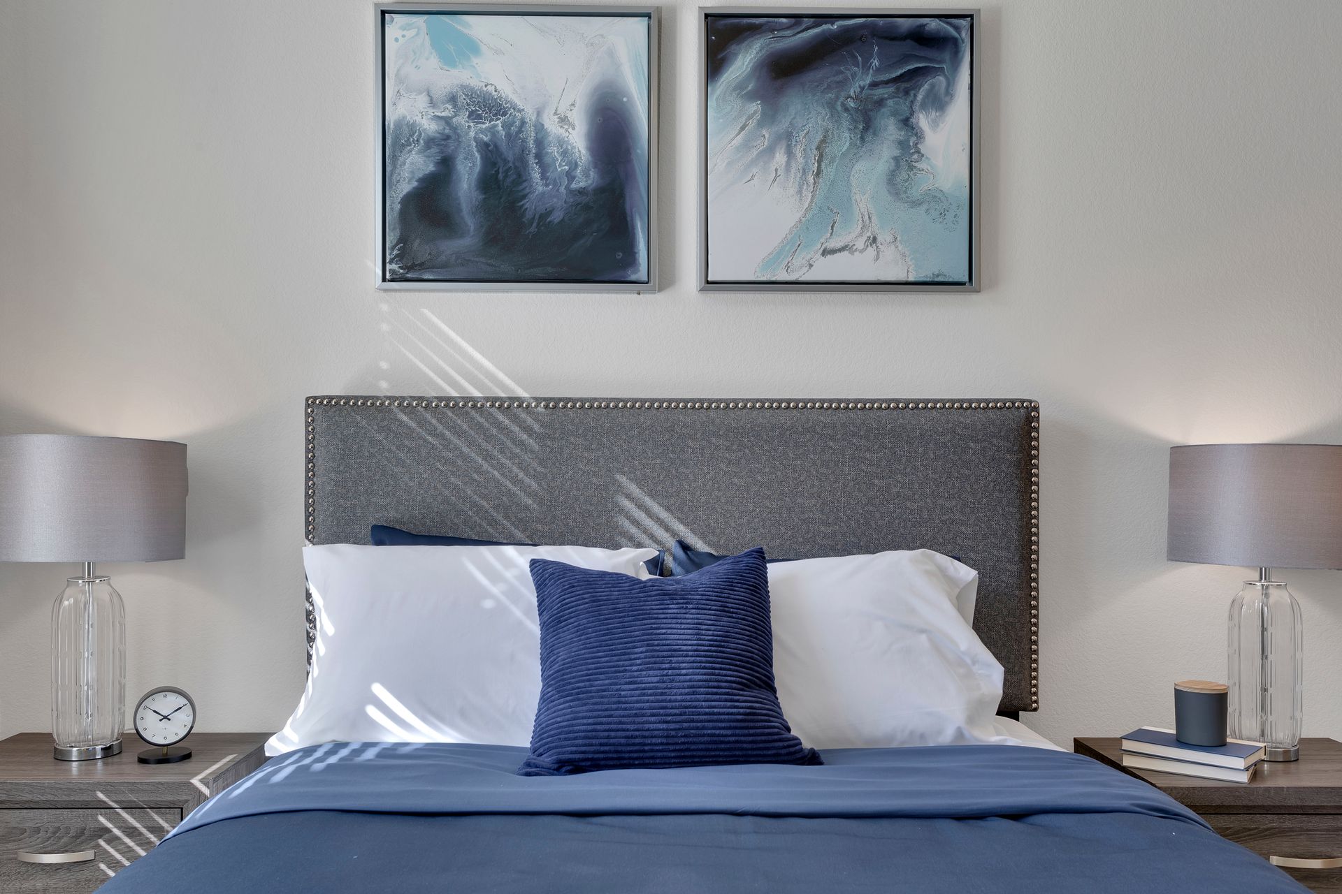 Modern bedroom with gray headboard, blue bedding, bedside lamps, and abstract wall art
