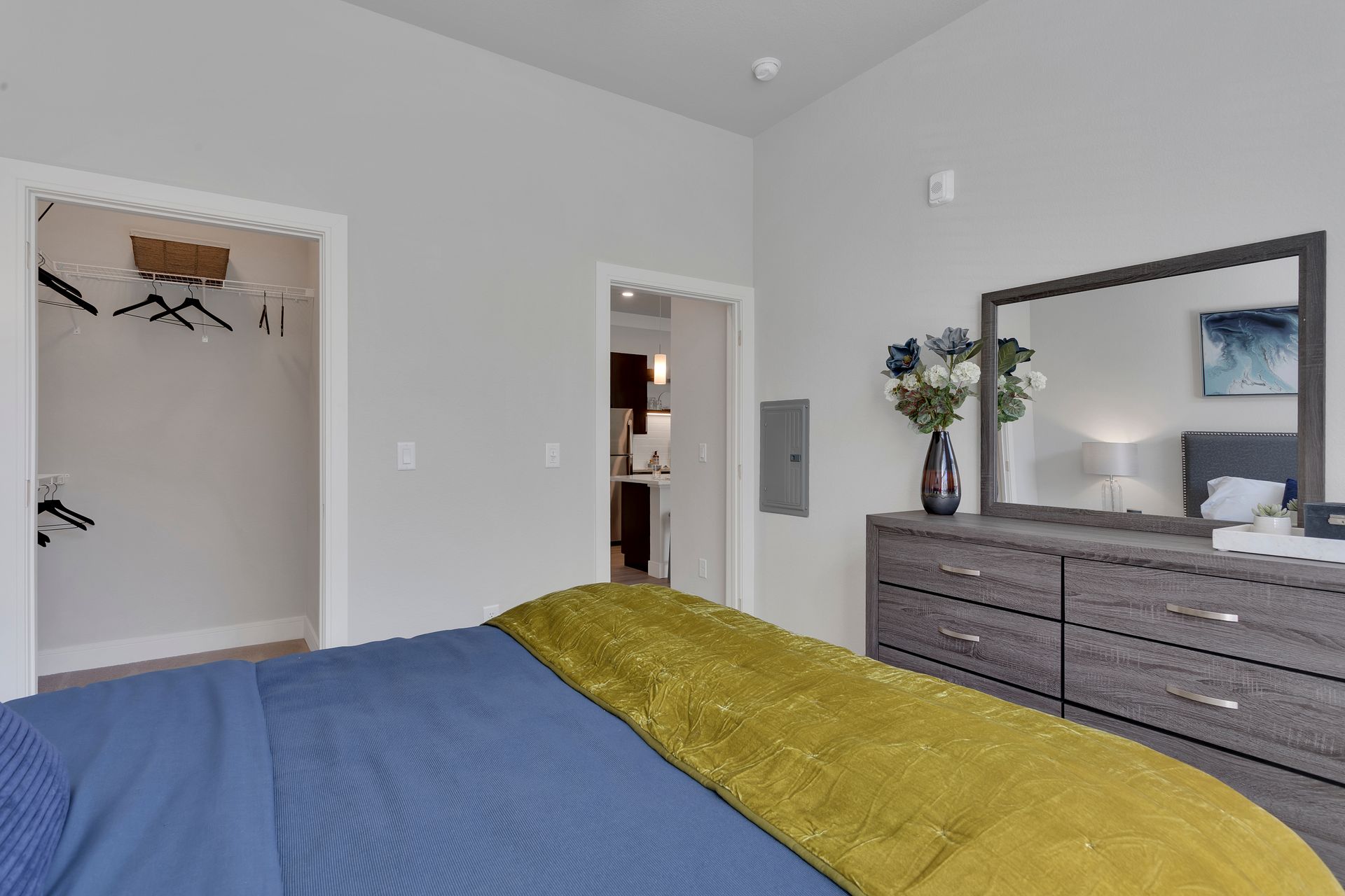 Bedroom with blue and mustard bedding, gray dresser with mirror, and open closet and doorway in view