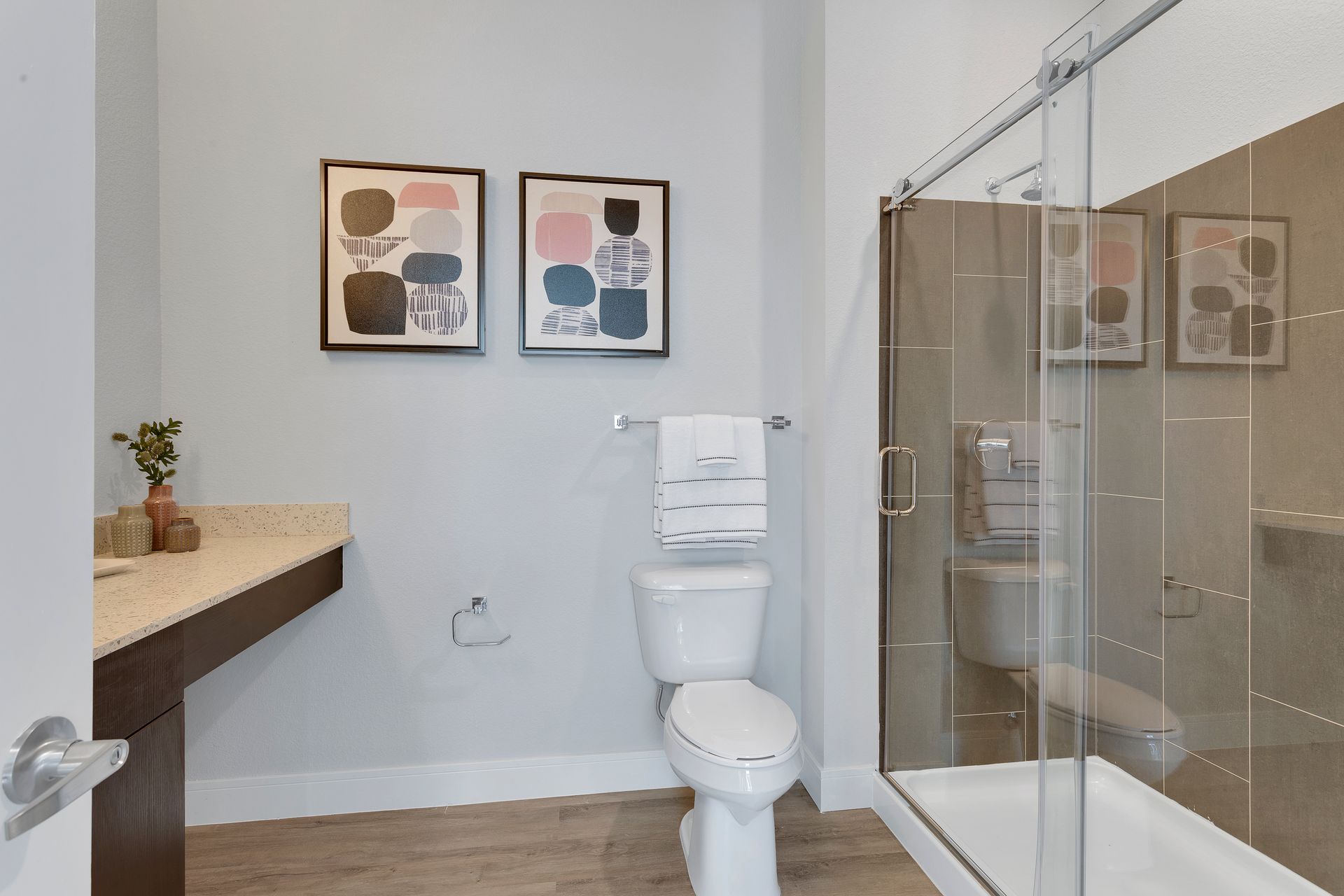 Small bathroom with toilet, glass shower, and wall art on a light gray wall