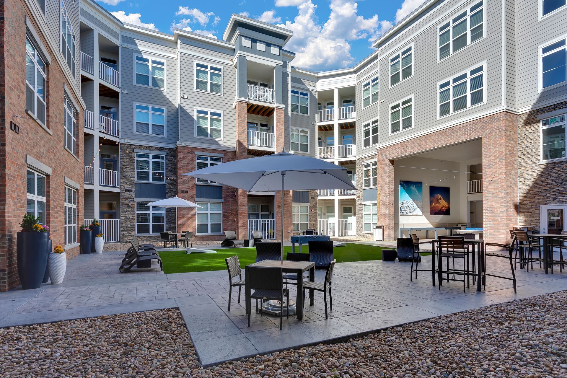 Courtyard with outdoor tables and umbrellas between brick apartment buildings under a blue sky