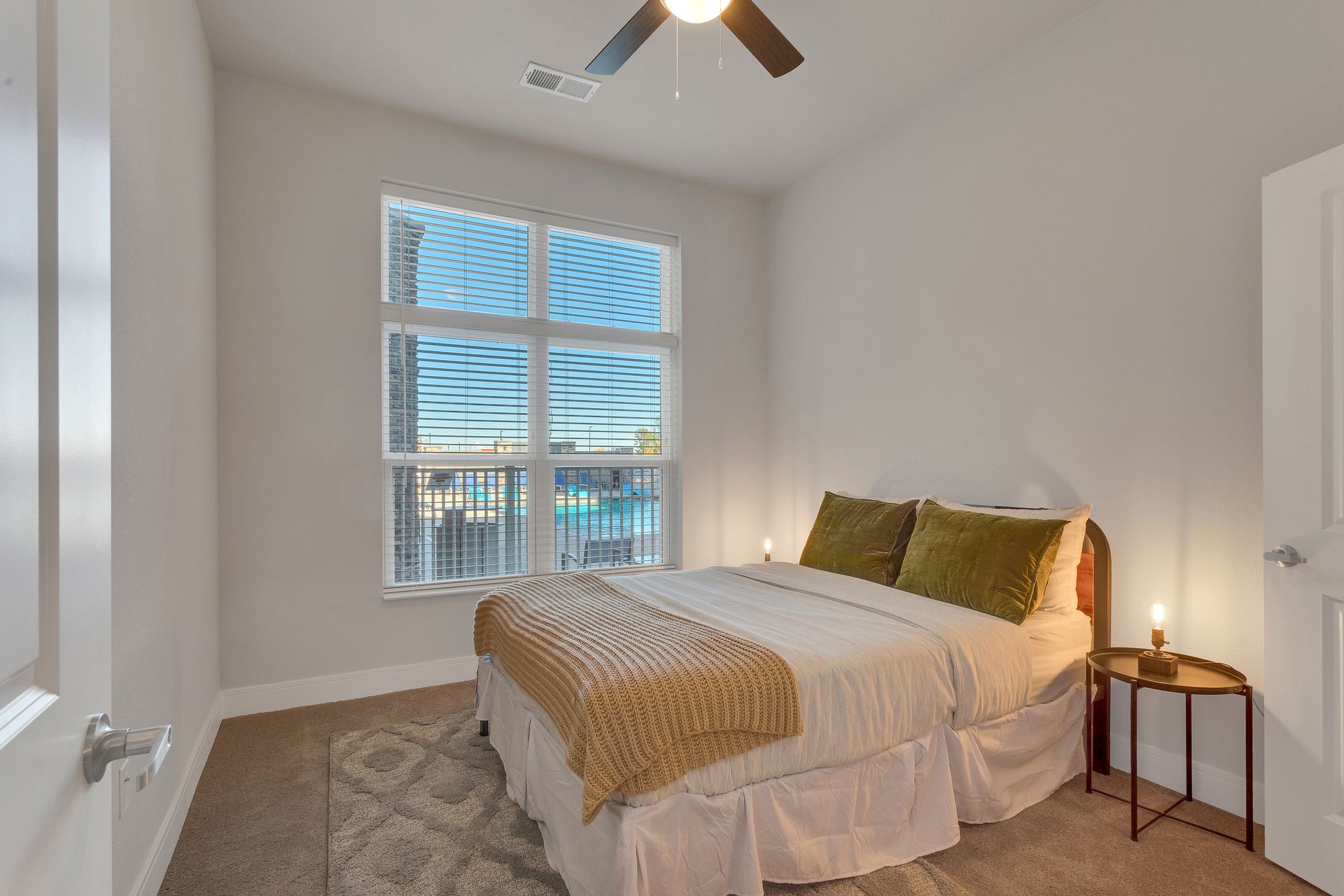 Bright bedroom with a bed, nightstand, ceiling fan, and window blinds letting in daylight