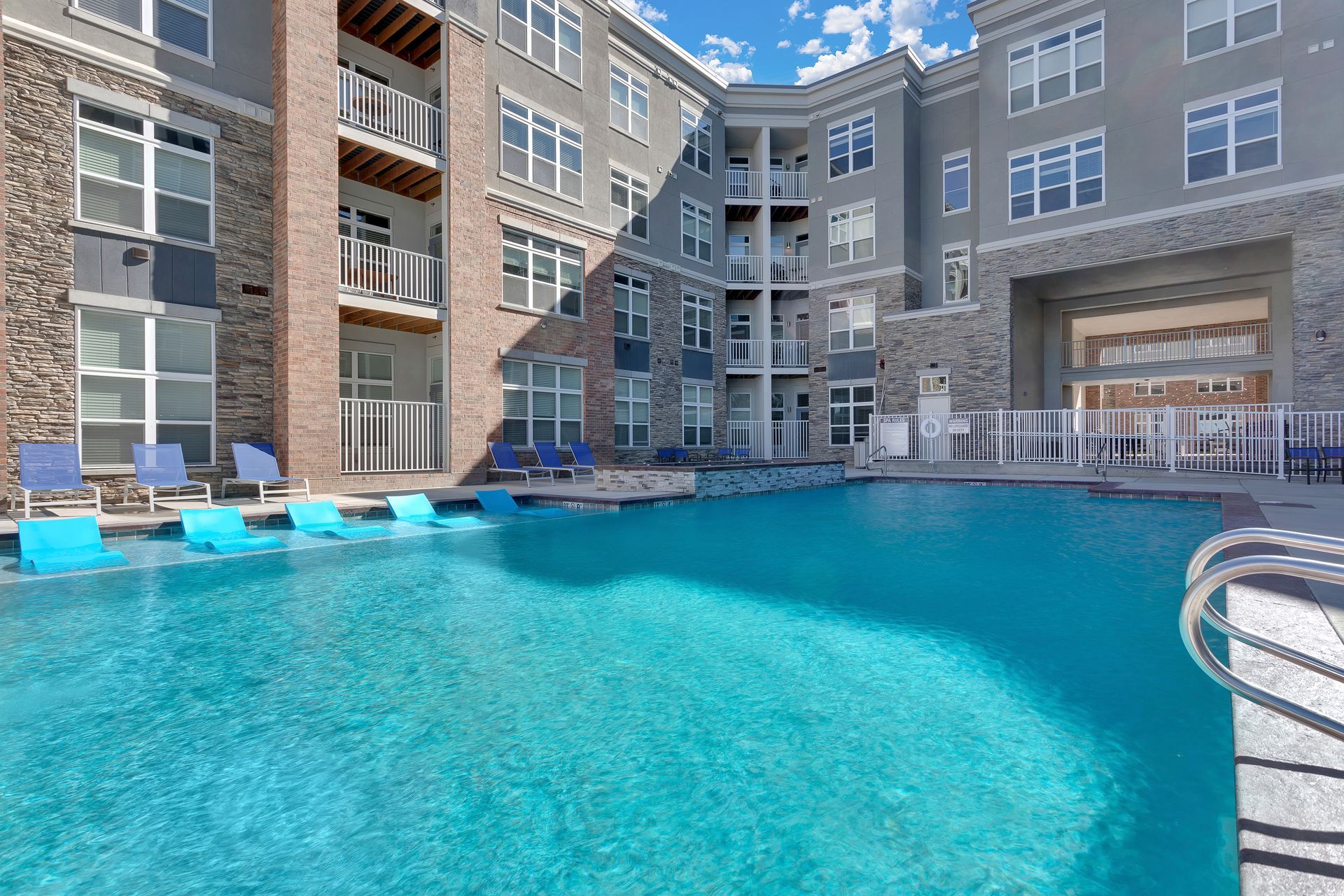 Apartment complex outdoor pool with clear blue water and lounge chairs surrounding it