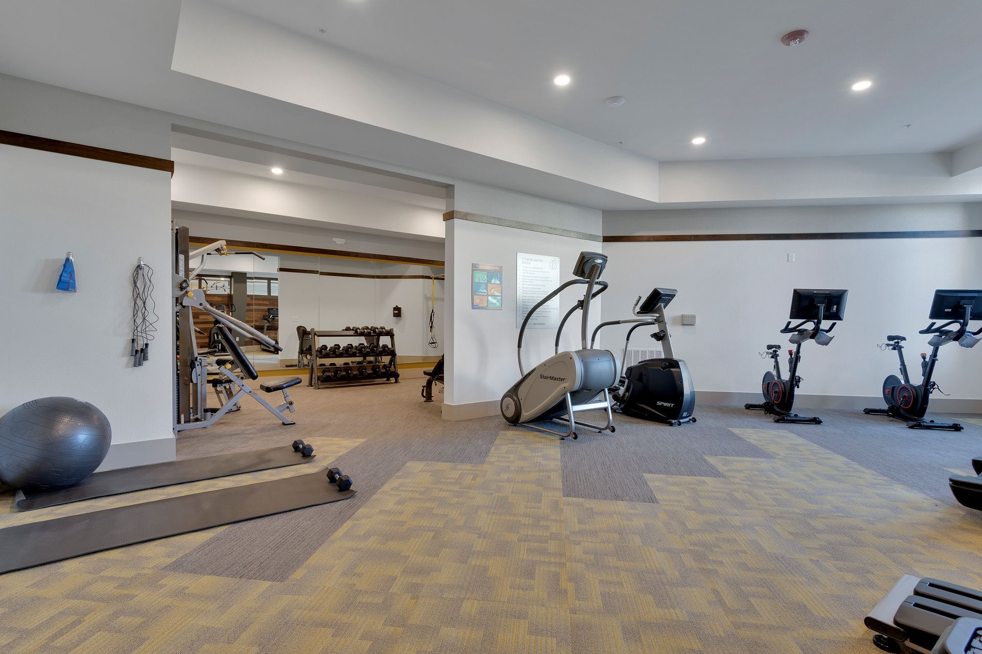 Modern gym with cardio machines, exercise equipment, and beige carpeted flooring