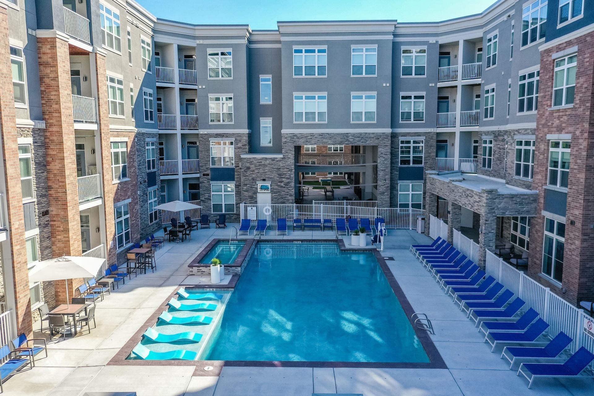 Apartment courtyard with a blue swimming pool, lounge chairs, and surrounding multi-story buildings