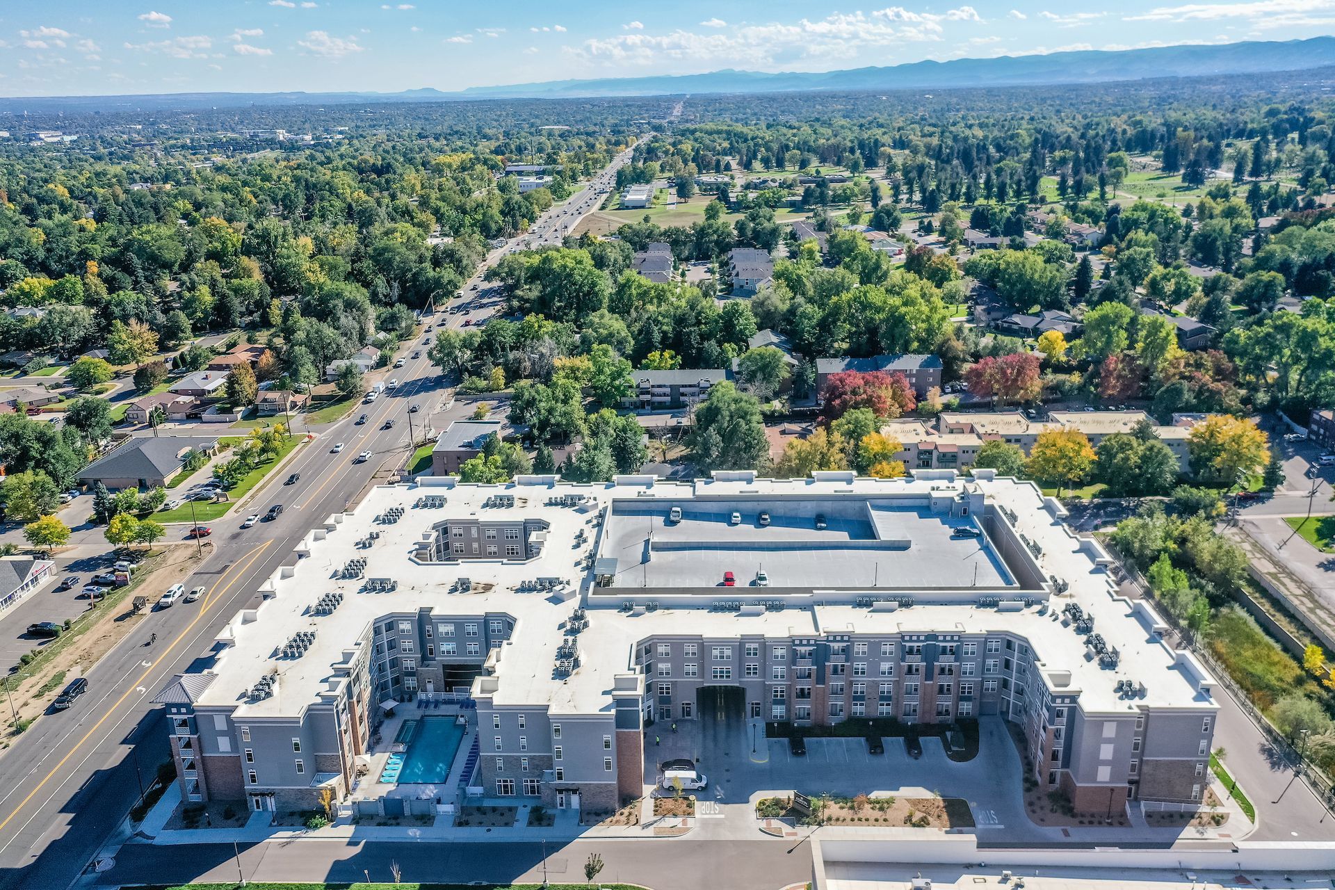 Aerial view of a large white apartment complex surrounded by trees in a suburban neighborhood.