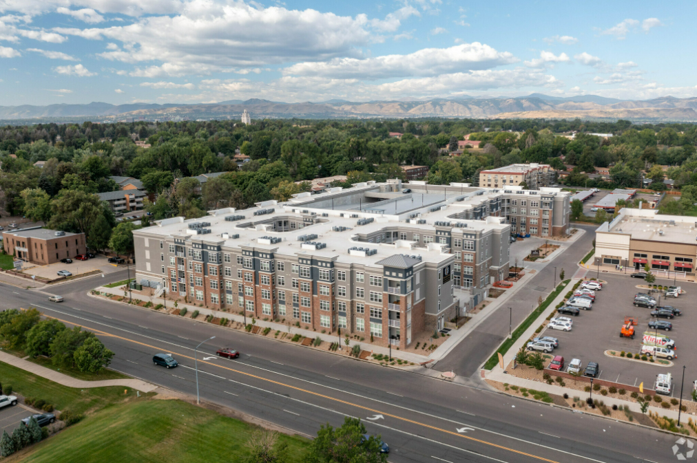 Aerial view of a modern apartment complex beside a busy road, with trees and mountains in the distance