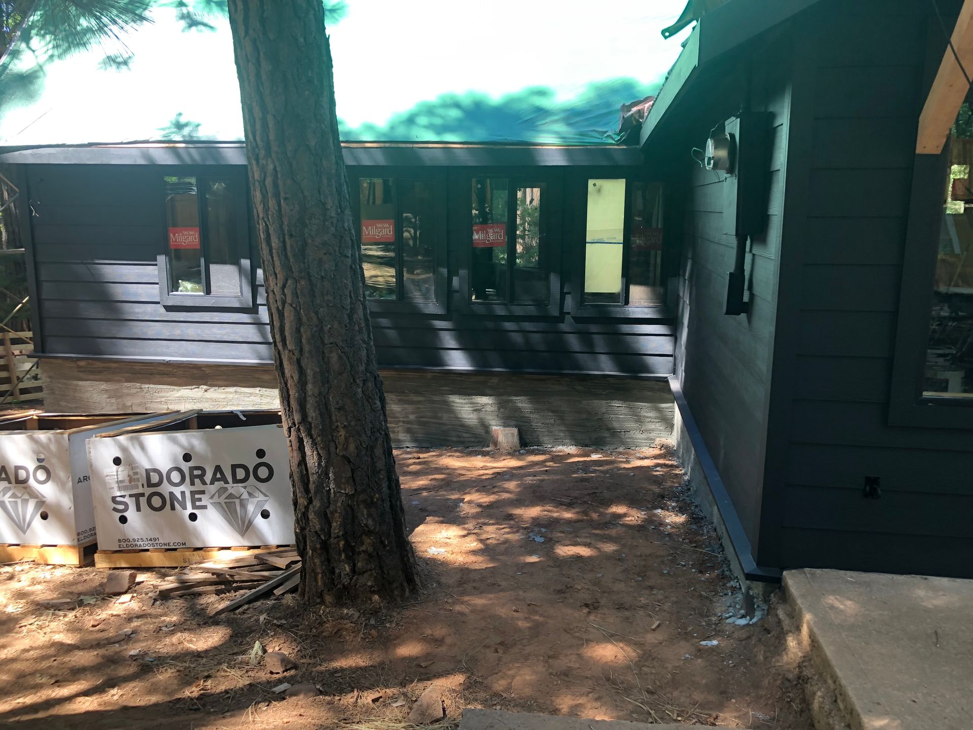 A dark-sided house exterior under construction with Eldorado Stone materials stacked near a large tree.