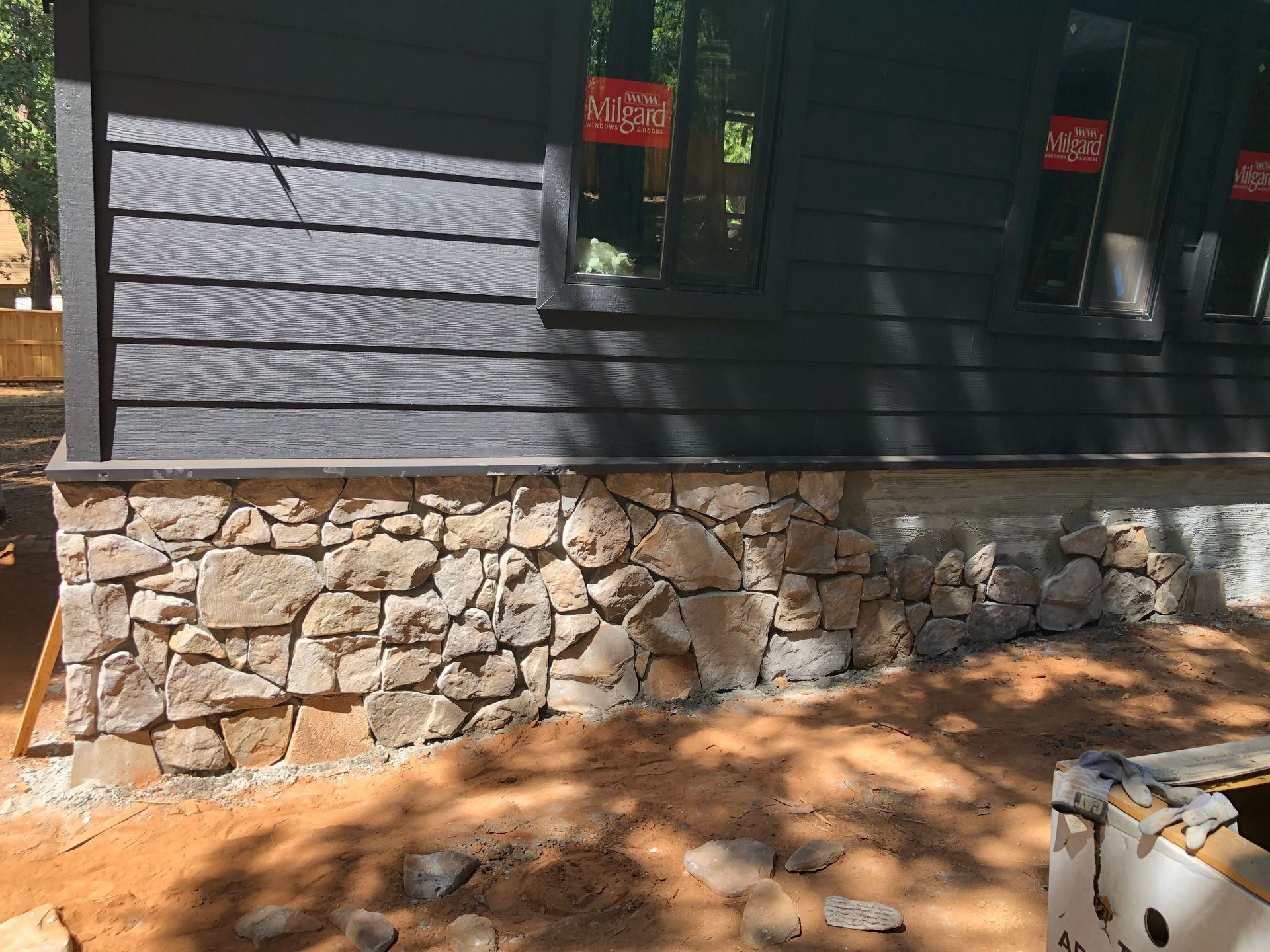A house exterior showing dark horizontal siding above a foundation wall made of natural, multicolored stone.