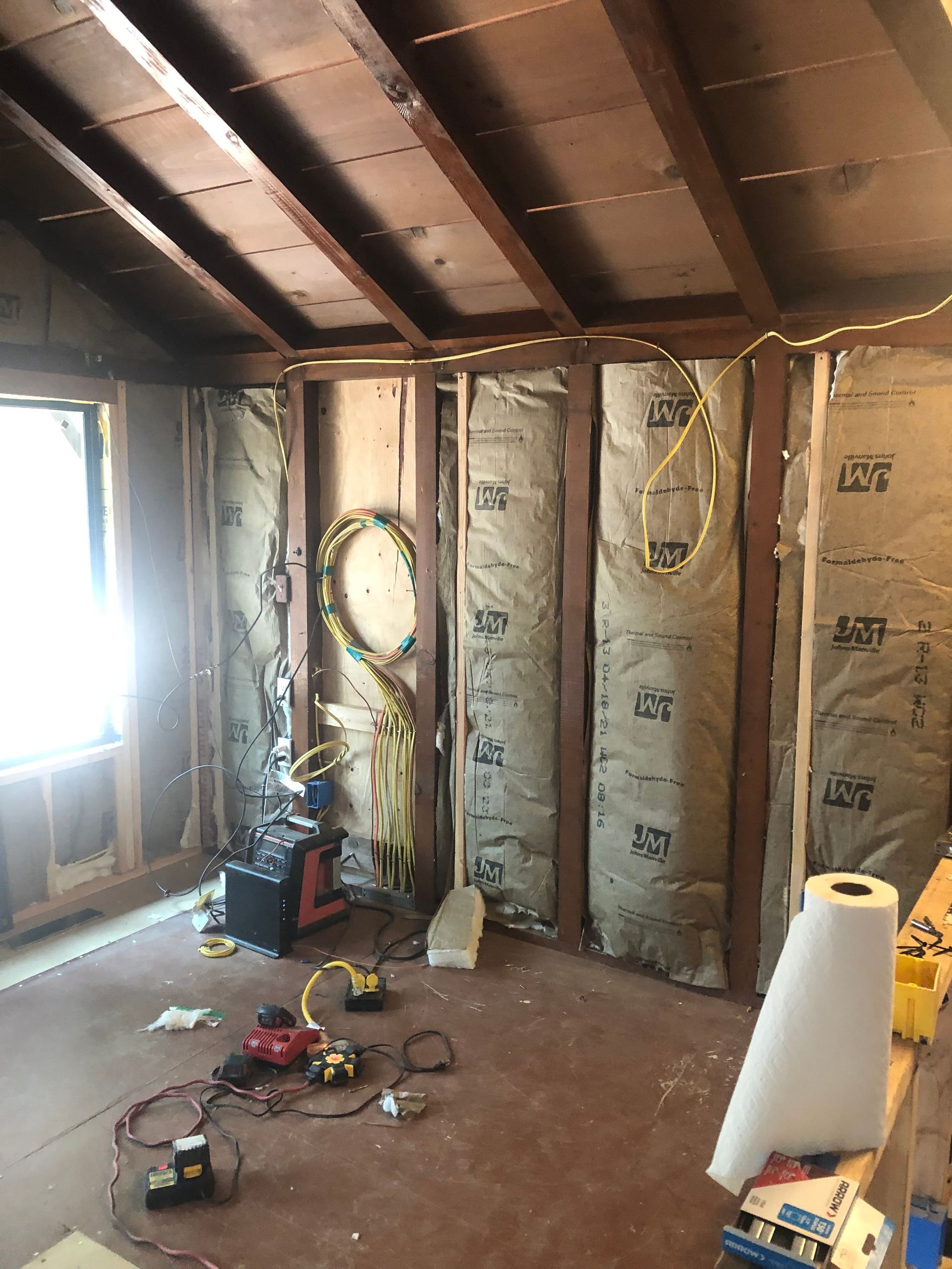 Interior of an unfinished room with exposed wood framing, insulation panels, and electrical wires scattered on the floor.