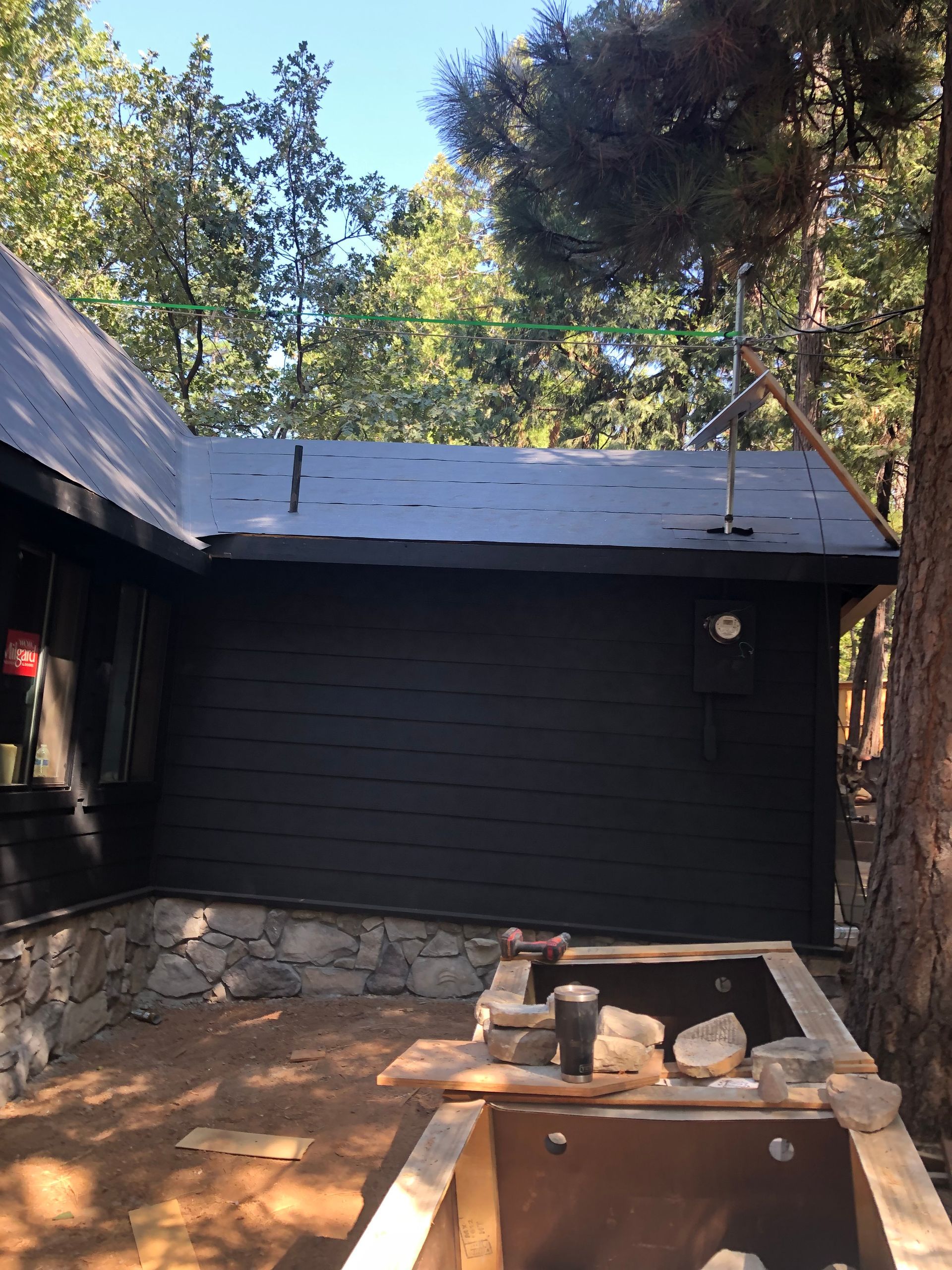 A house exterior with black siding and stone foundation, next to an outdoor construction area with stone materials.