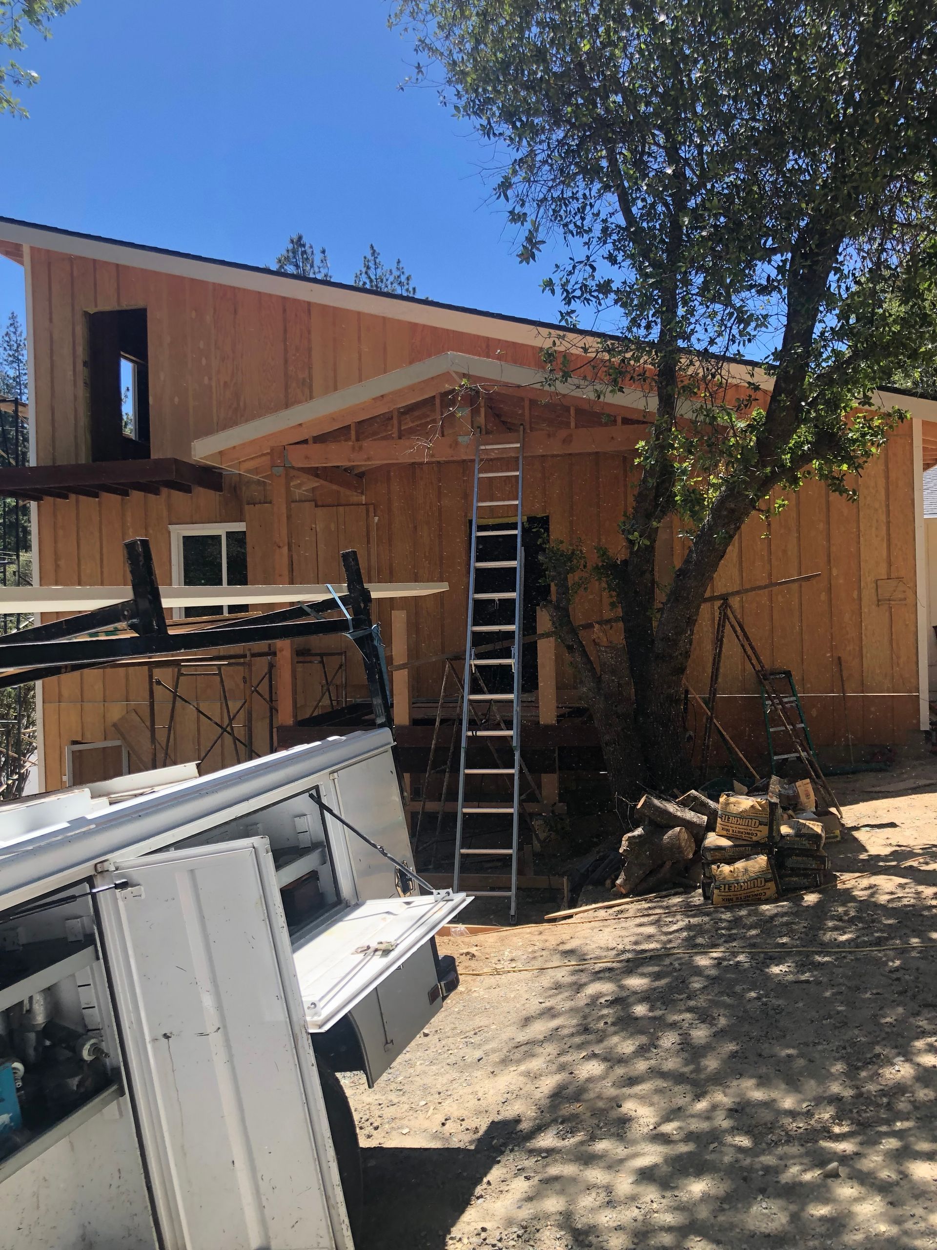 A house under construction with raw wood siding, a wooden front porch frame, and a ladder leaning against it.