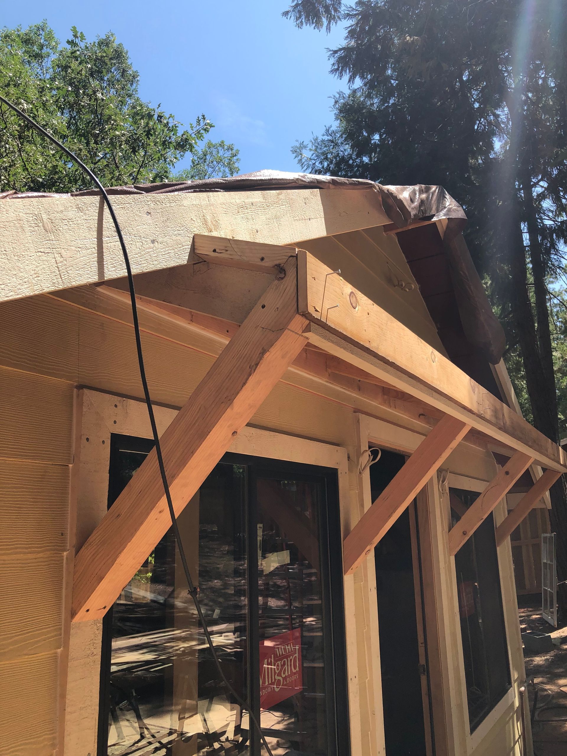 A low-angle view of a wooden shed under construction, showing a newly framed entryway roof against a clear blue sky.
