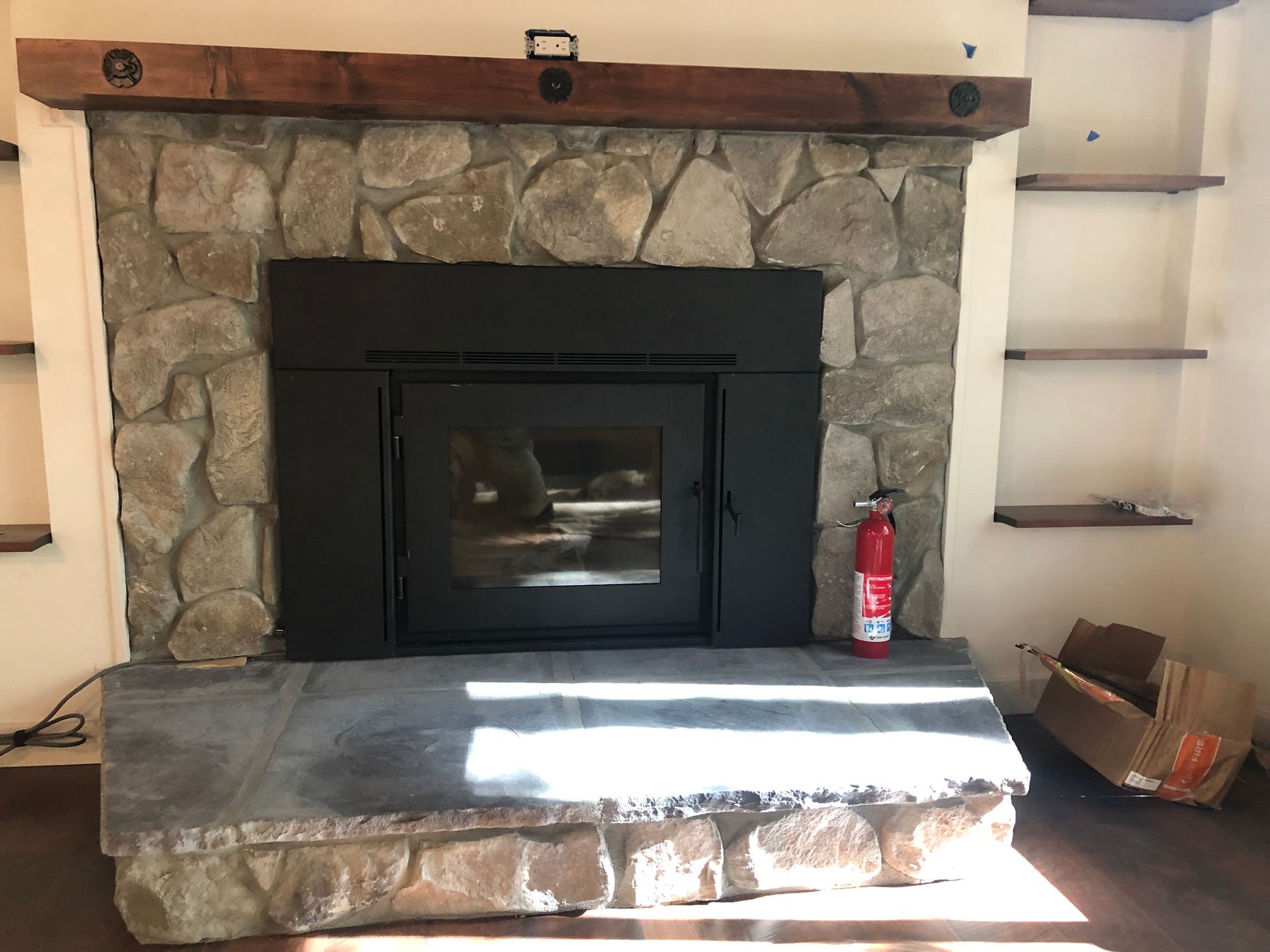 A stone fireplace with a black insert, wooden mantel, and flagstone hearth, flanked by built-in shelves.