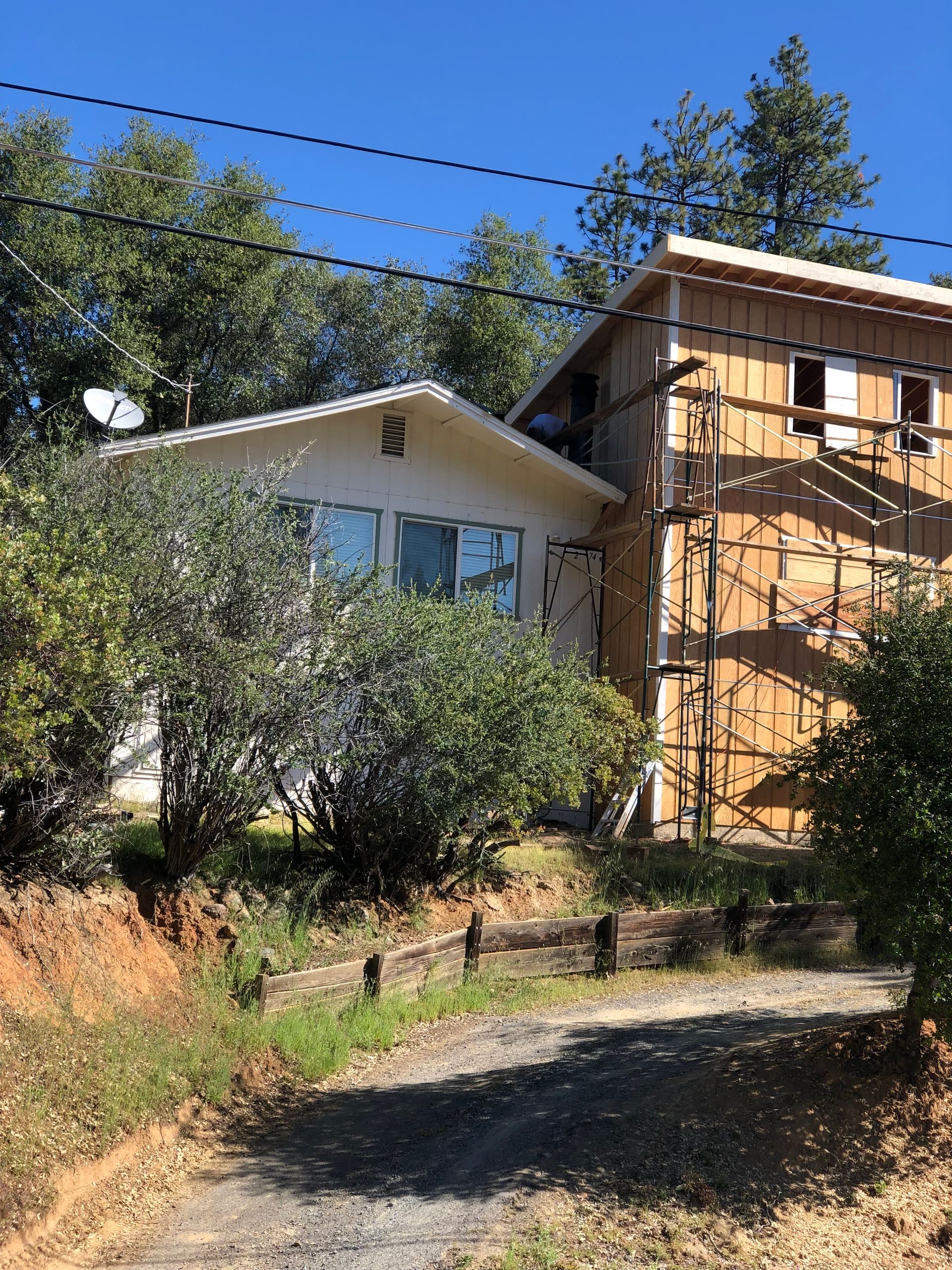 A house under construction with scaffolding against a two-story wood-sided section and a light-colored single-story wing.