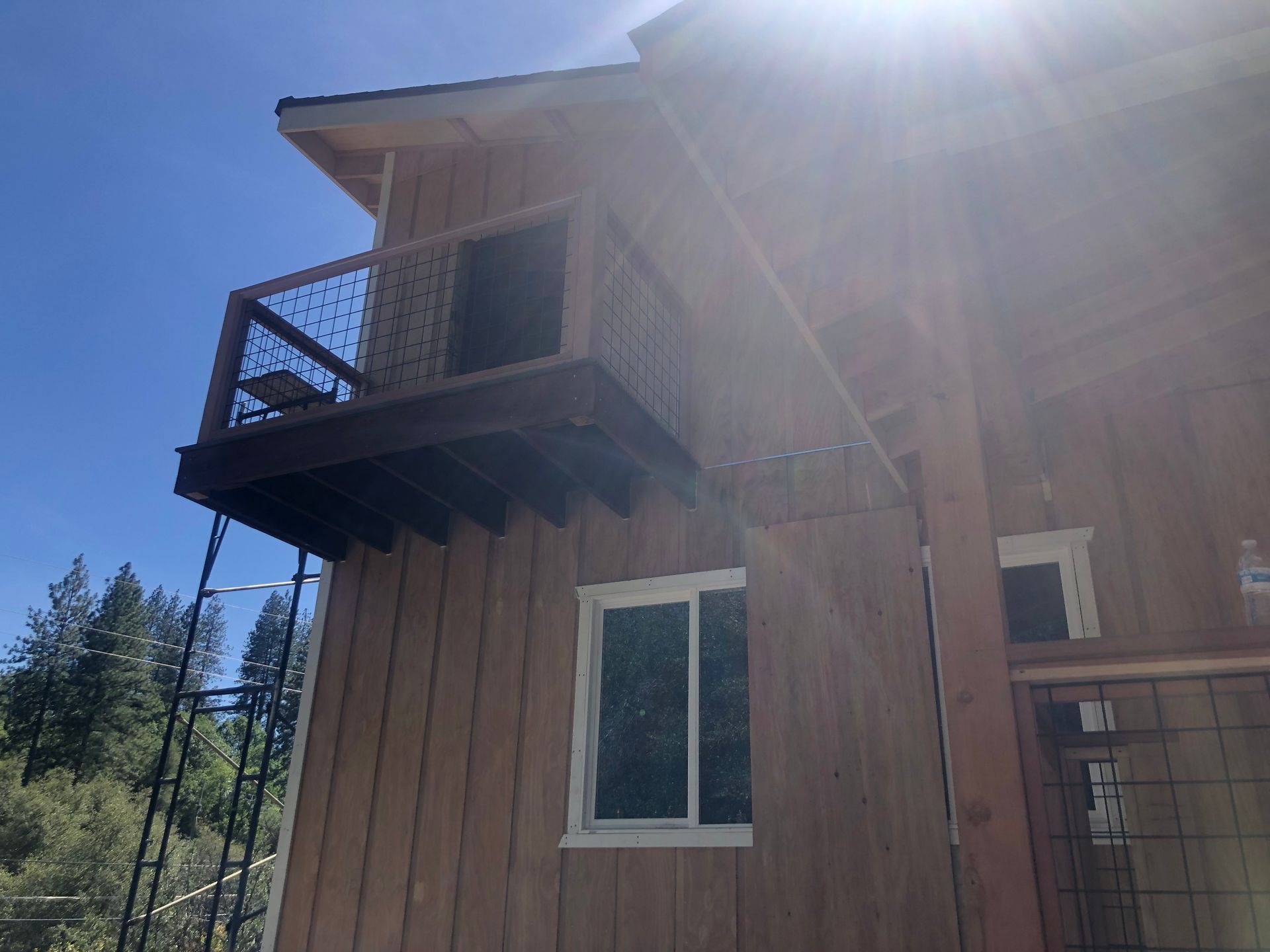 A wooden exterior wall with a small elevated balcony featuring wire-mesh railings, set against a bright, sunny sky.